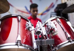 Unrecognizable Afro boy with red jacket attending a drum class and playing